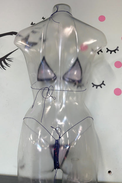 A clear, transparent plastic torso mannequin wearing a matching sheer lingerie set with dark blue/purple trim, photographed against a white wall with decorative eyelashes and pink dots.
