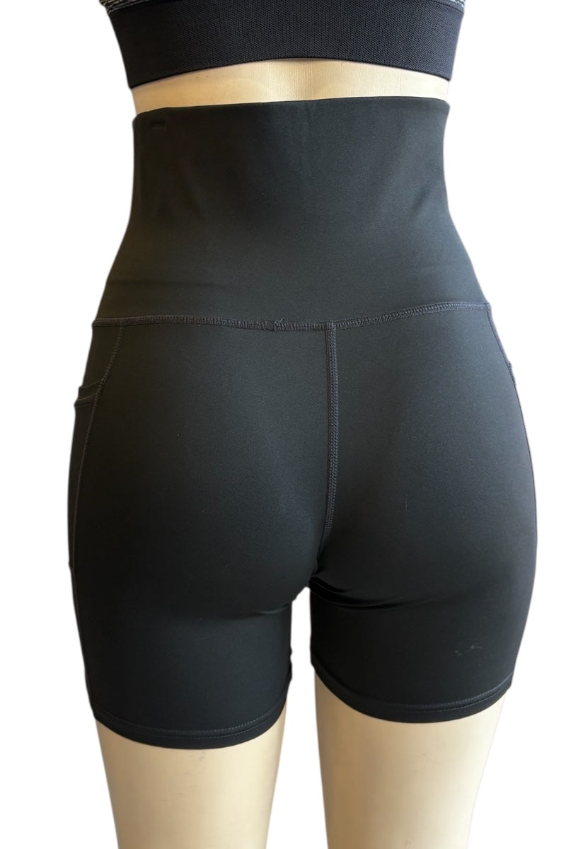 Black high-waisted athletic biker shorts shown from the back on a mannequin, with a matching black sports bra partially visible at the top against a plain white background.