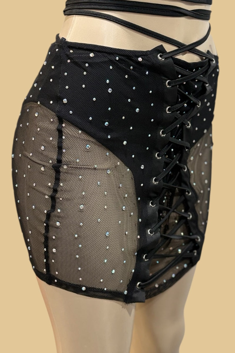 Black mesh skirt with lace-up front and rhinestone embellishments on a beige background