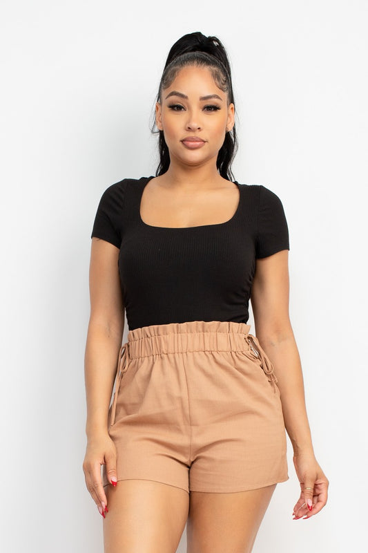 Woman wearing a black top and beige shorts on a white background
