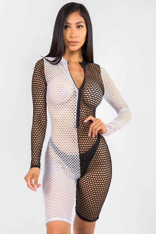 A woman modeling a long-sleeve, bodycon fishnet romper with a split black and white design on a light gray studio background.