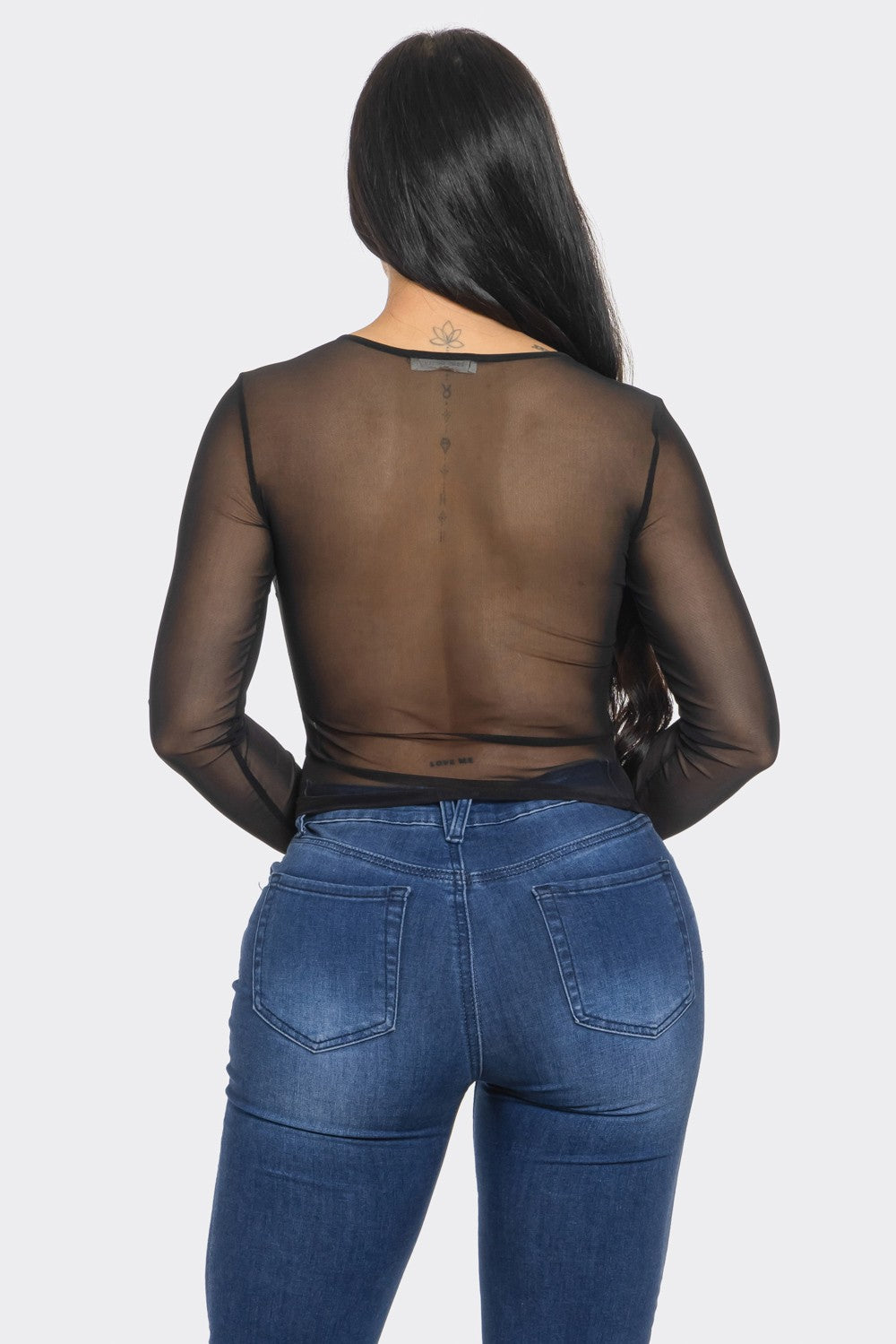 Person wearing a sheer black top and blue jeans on a white background