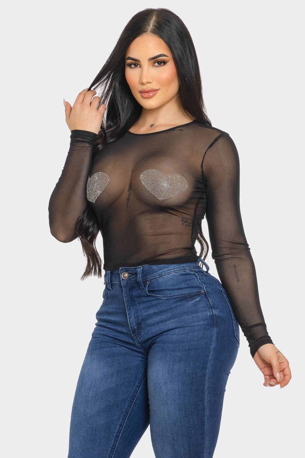 Woman wearing a sheer black top with heart designs and blue jeans on a white background
