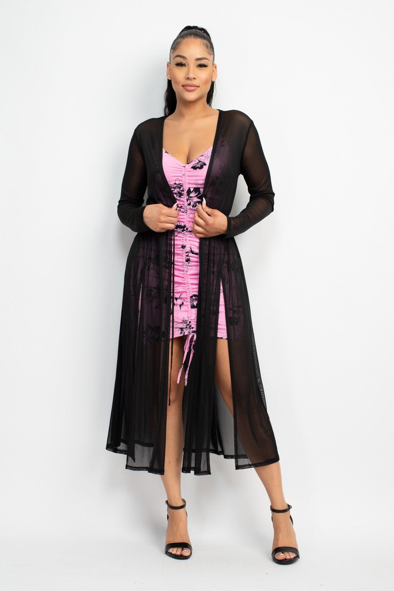 Woman wearing a pink dress with a black sheer cover-up on a white background