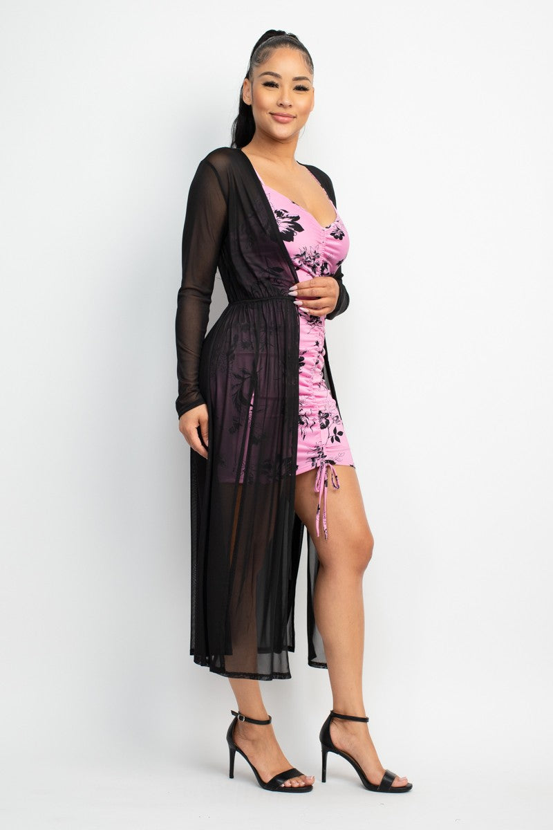 Woman wearing a pink floral dress with a sheer black overlay on a white background