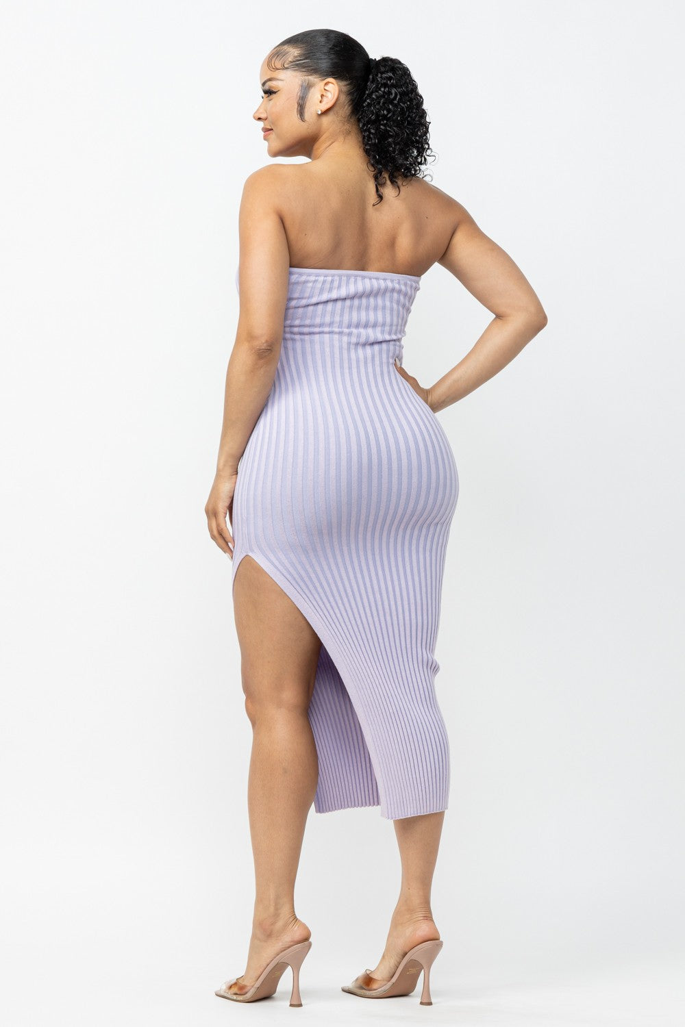 Woman wearing a lavender strapless ribbed dress with a high slit on a white background