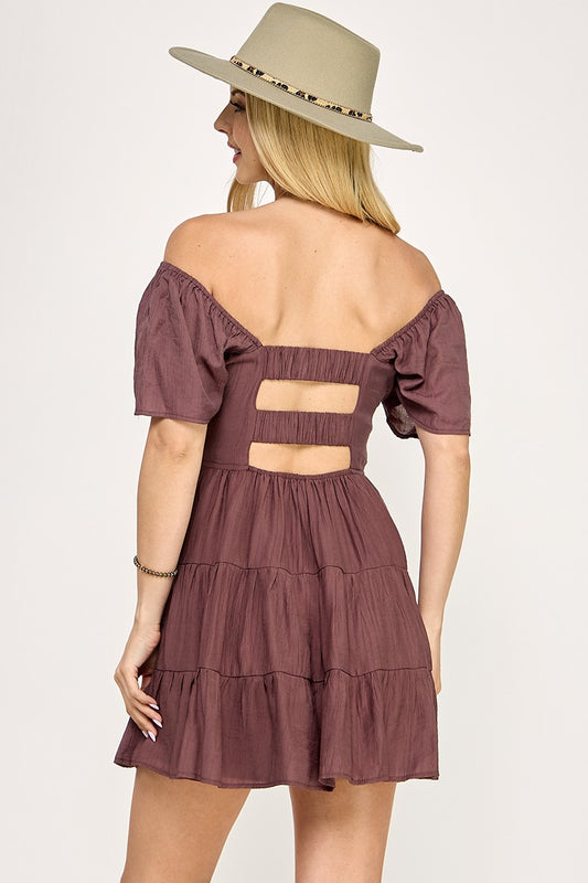 Woman wearing a brown off-shoulder dress with cut-out details and a beige hat on a white background
