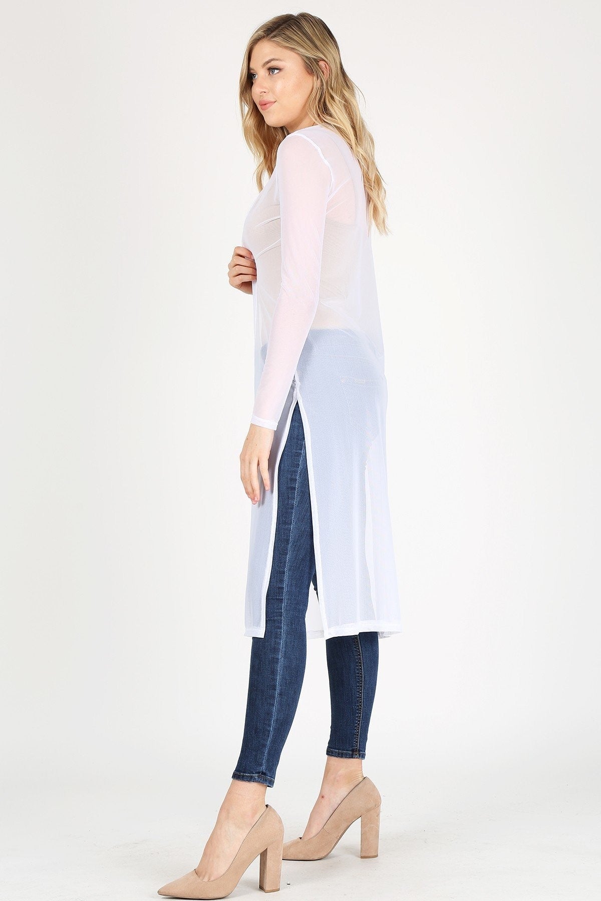 Woman wearing a long, sheer white cardigan paired with dark jeans on a white background.
