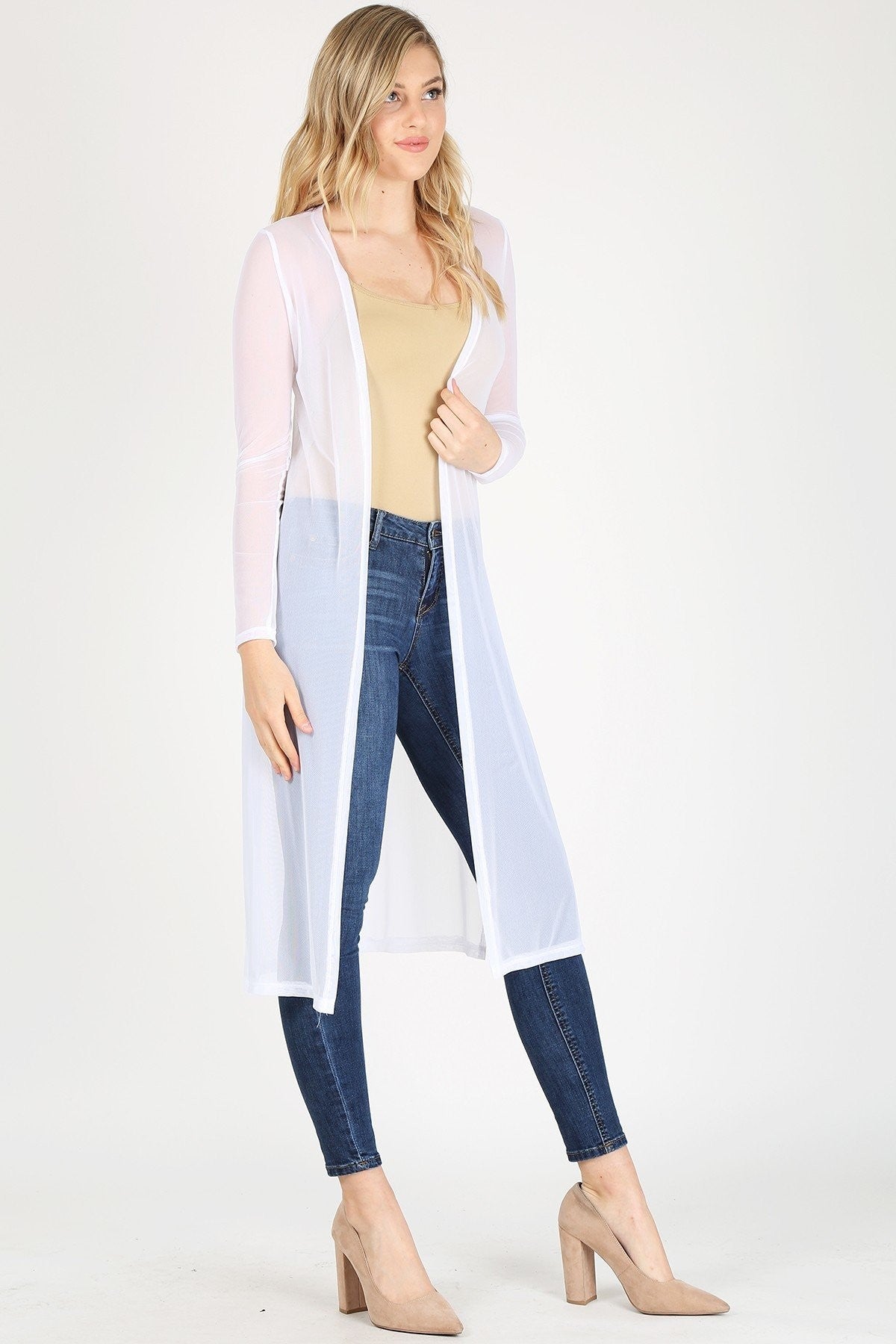 Woman wearing a white long cardigan over a beige top and blue jeans on a white background