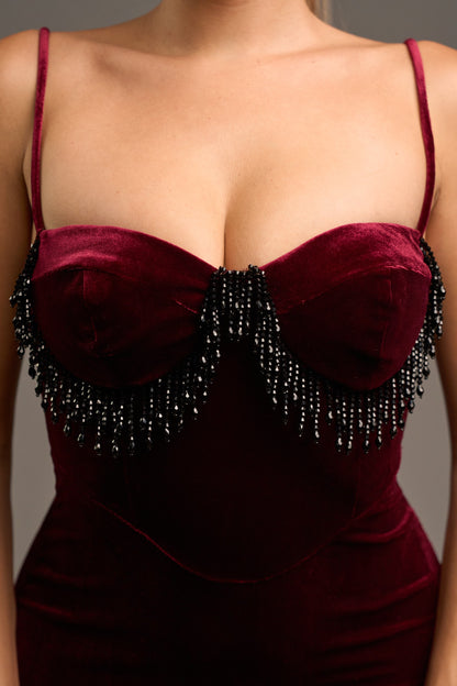 Close-up of a sangria color velvet dress with beaded details on a neutral background