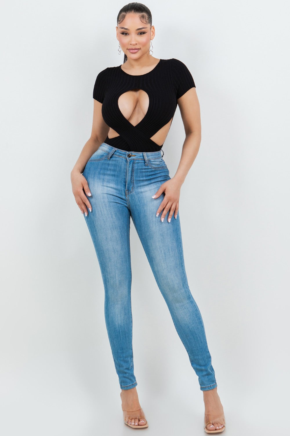 Woman wearing a black cut-out top and blue jeans on a white background