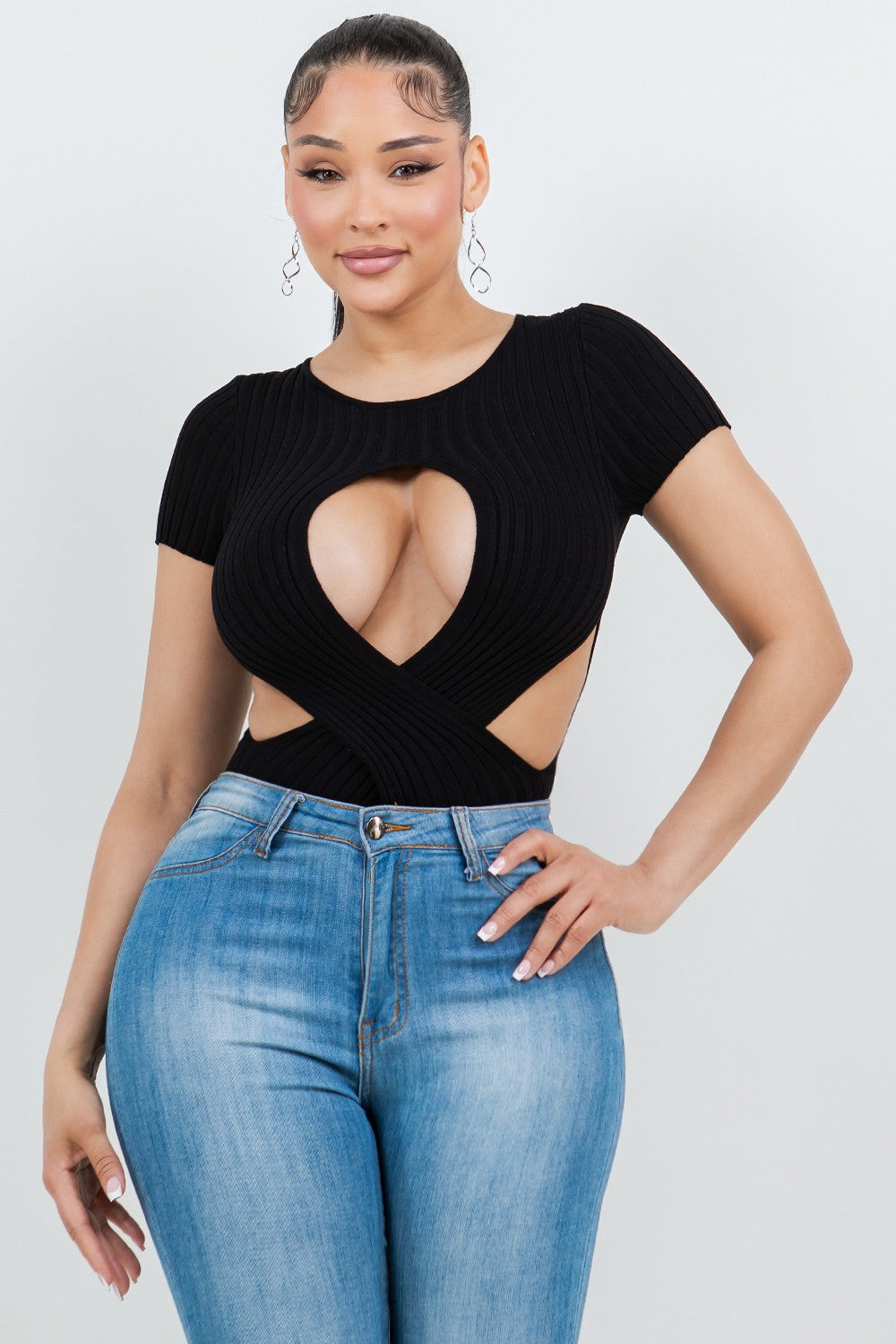 Woman wearing a black ribbed top with cut-out design and blue jeans on a white background