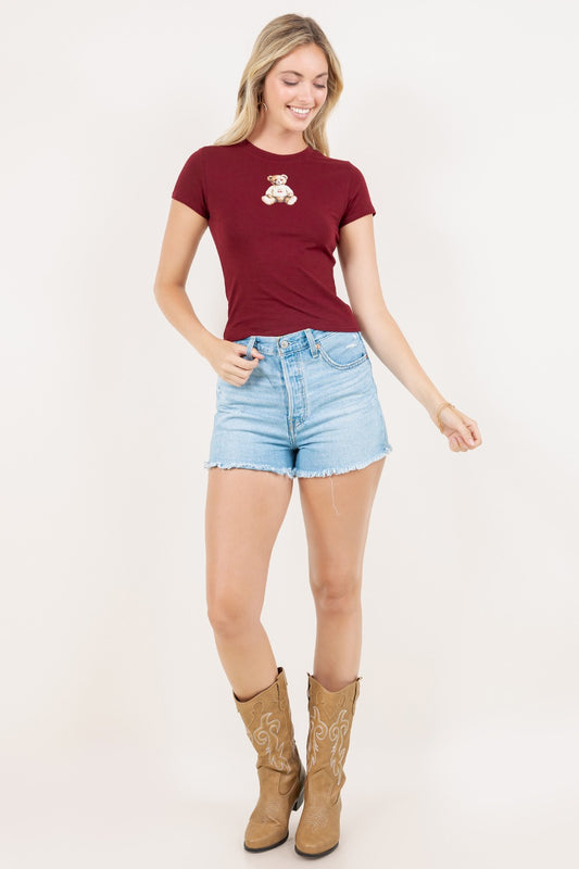 Woman wearing a burgundy t-shirt with a graphic, light blue shorts, and tan boots on a white background