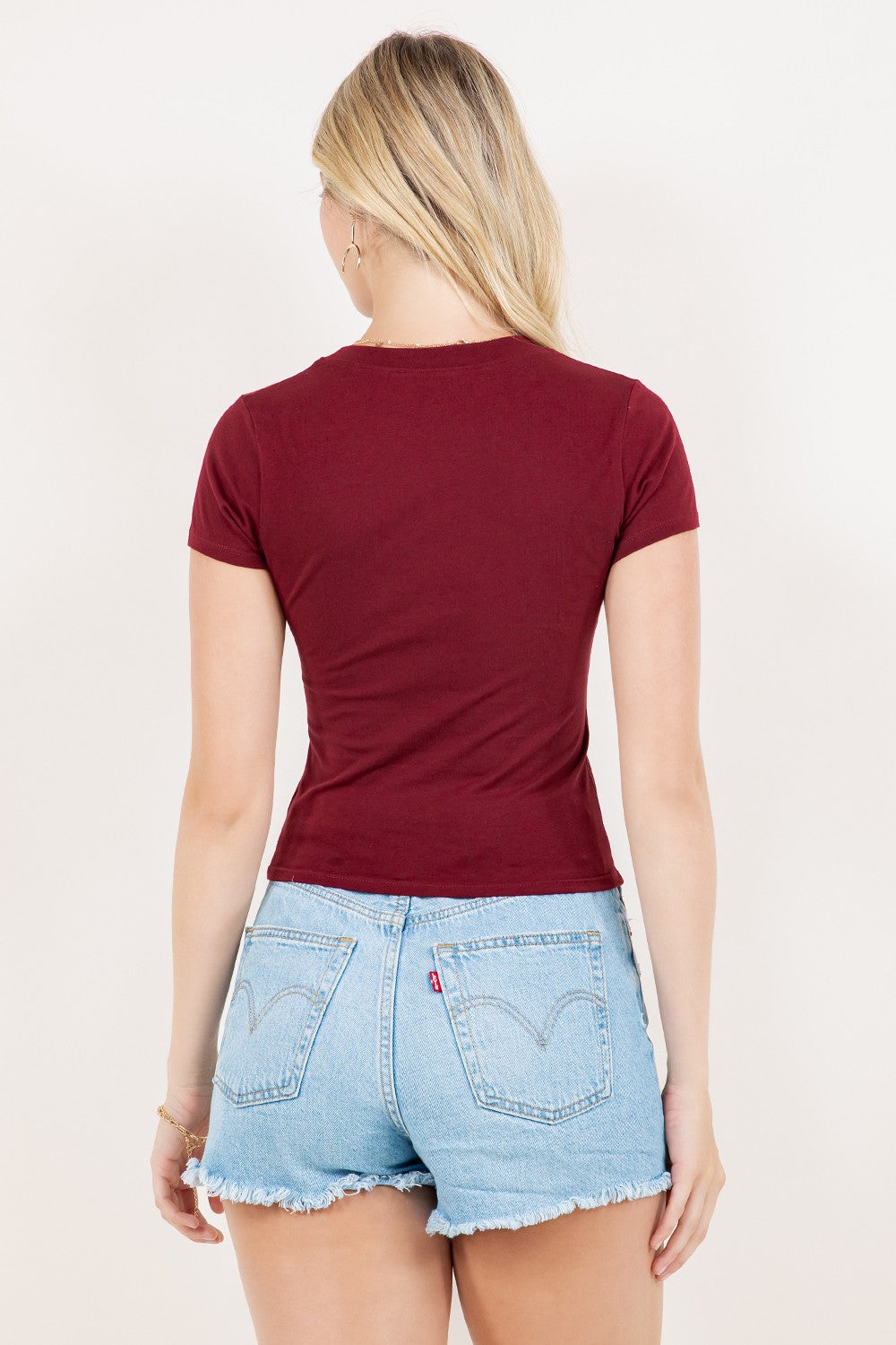 Person wearing a burgundy t-shirt and denim shorts on a plain background
