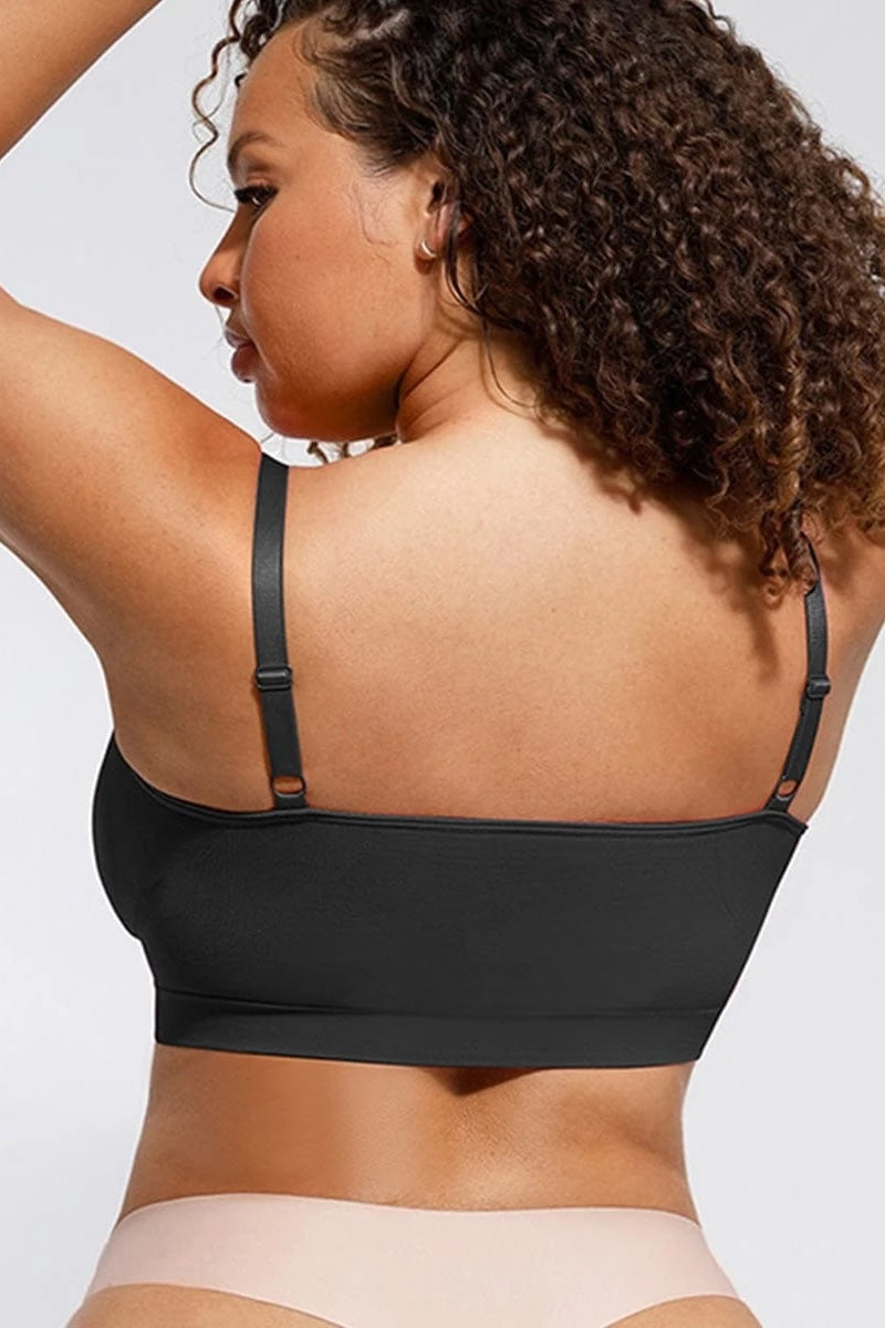 Woman wearing a black bralette and beige underwear on a light gray background