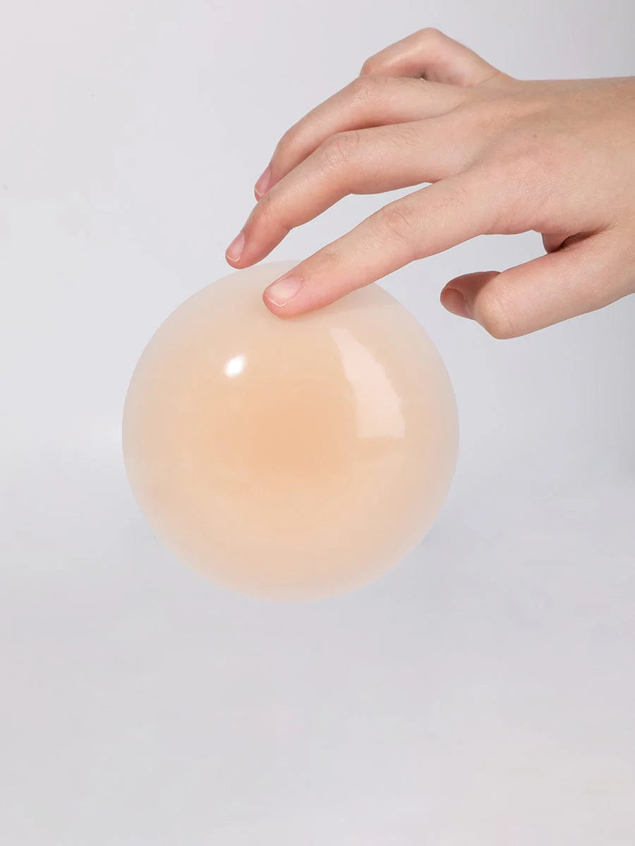 Hand touching a smooth, beige nipple cover on a light gray background