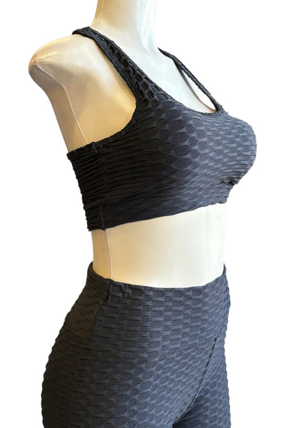Black textured sports bra and matching high-waisted leggings set displayed on a beige mannequin torso against a white background.