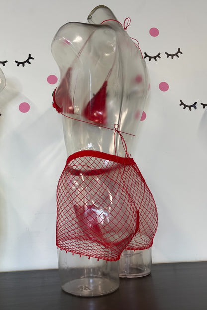 Red fishnet lingerie set consisting of a halter bra and matching mesh briefs, displayed on a clear plastic torso mannequin against a white wall with decorative eyelashes and pink dots.