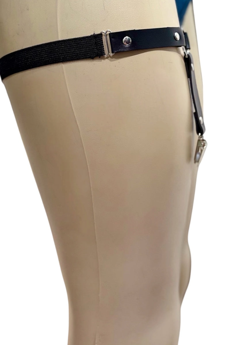 A black elastic thigh strap with silver metal snaps and adjusters, shown attached to a beige mannequin leg against a white background.