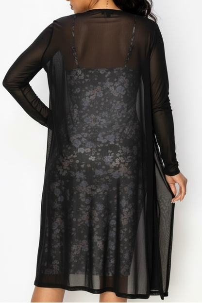 Black cardigan with sheer long sleeves over a floral dress on a model on a white background
