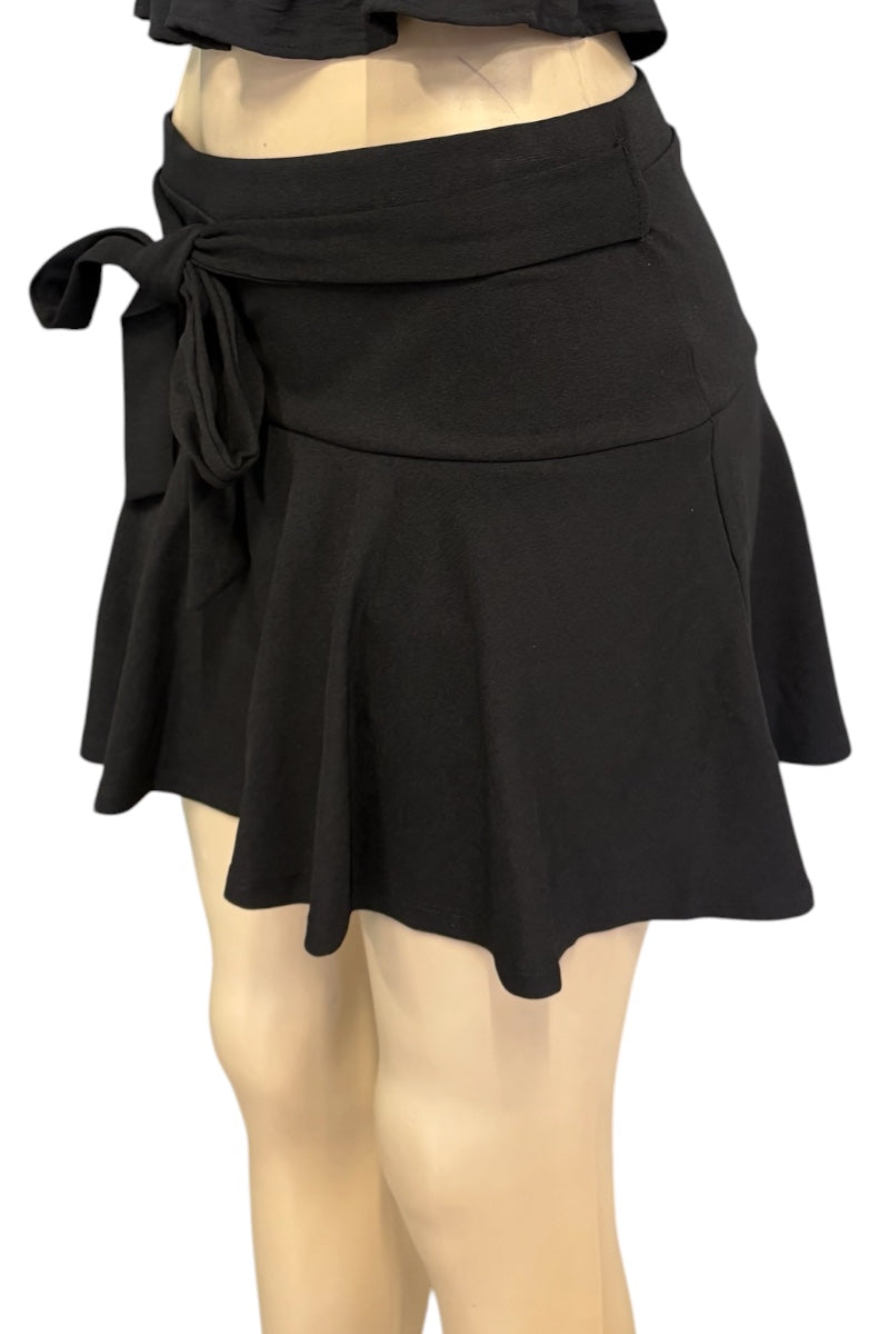 A black wrap-style mini skirt with a tied waist and flared ruffled hem, displayed on a beige mannequin against a plain white background.
