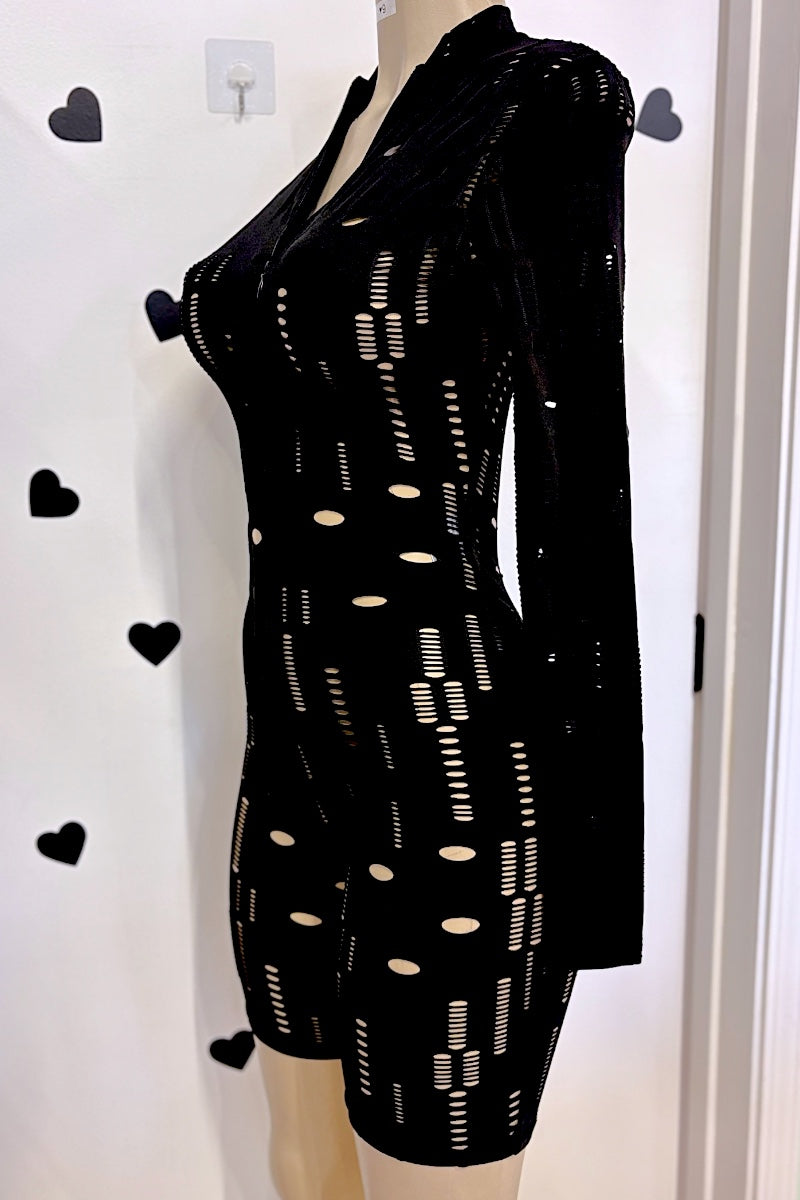 A black long-sleeve romper with a sheer mesh pattern and vertical dotted cutouts, displayed on a mannequin against a white wall with heart-shaped decorations.