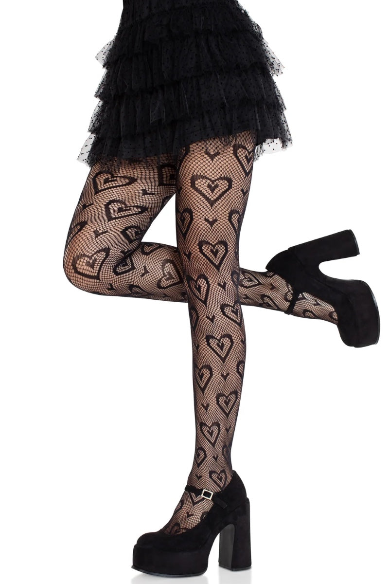 Black heart-patterned fishnet tights worn by a model, paired with a black ruffled skirt and black platform heels, shown against a plain white background.