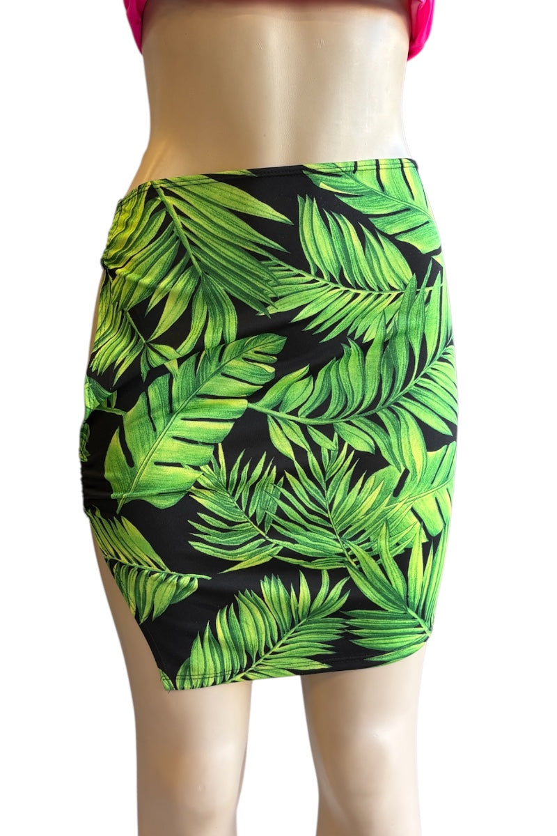 A bodycon mini skirt with a vibrant green tropical palm leaf pattern on a black background, displayed on a mannequin torso.