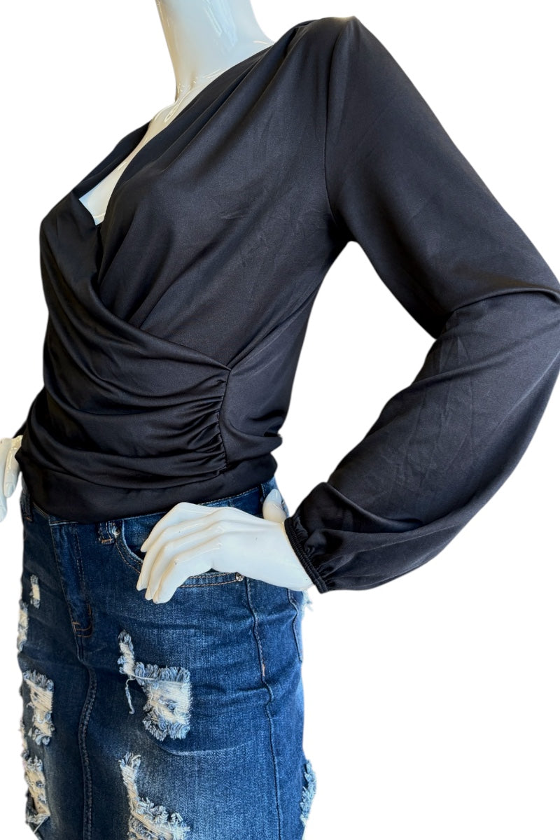 A black long-sleeve wrap-style top with a ruched waist, displayed on a mannequin torso paired with a distressed blue skirt against a plain white background.