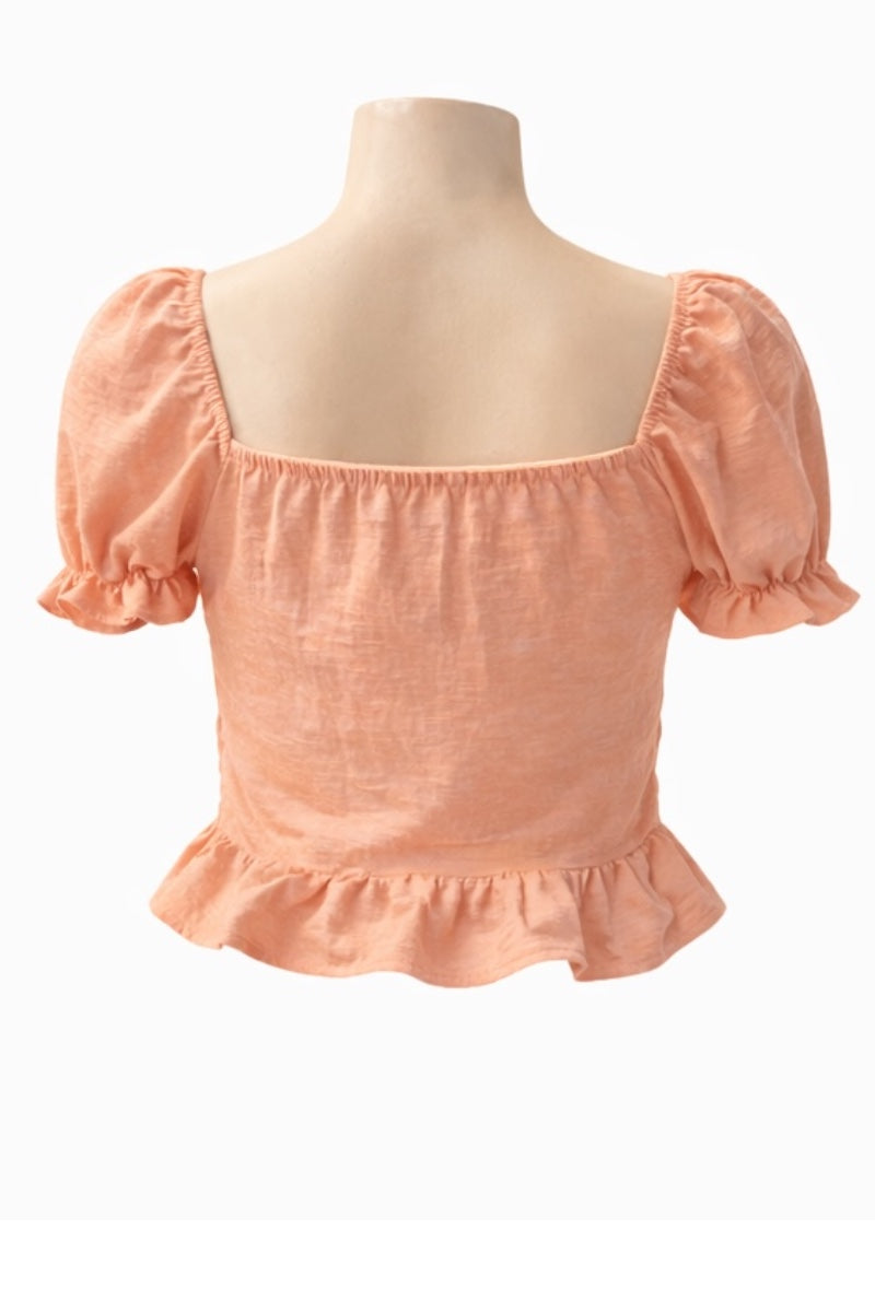 pink coral-colored blouse with ruffled sleeves and hem on a mannequin against a white background