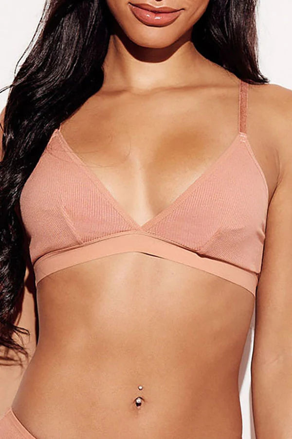 A close-up of a woman wearing a ribbed, peach triangle bralette with thin straps and a crossover band across the bust.