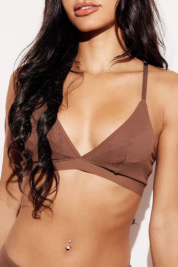 A close-up of a woman wearing a brown ribbed triangle bralette with thin shoulder straps and a crossover underband, shown against a plain light background.
