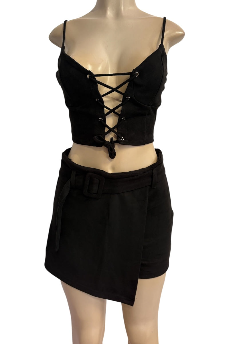 A black two-piece outfit displayed on a beige mannequin, featuring a lace-up corset-style top with thin straps and a matching asymmetrical mini skirt with a belt.