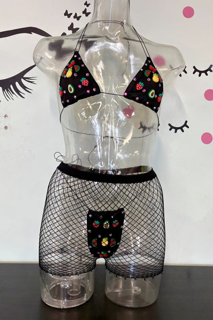 Black bikini and fishnet mini shorts set with colorful charms, displayed on a clear plastic mannequin torso against a white wall with decorative eyelashes and pink dots.