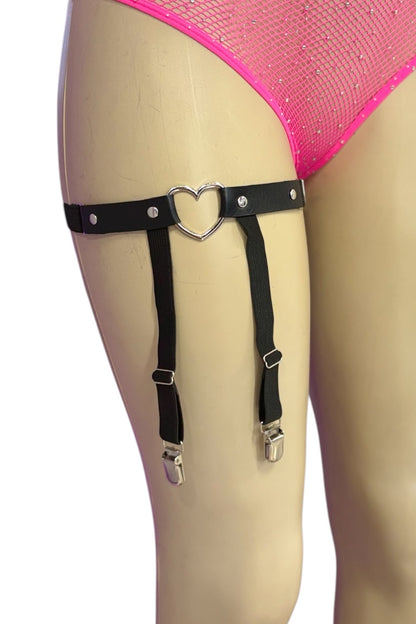 Black faux leather leg garter with a heart-shaped metal ring with adjustable straps with silver snap hooks, displayed on a beige mannequin leg wearing pink mesh underwear.