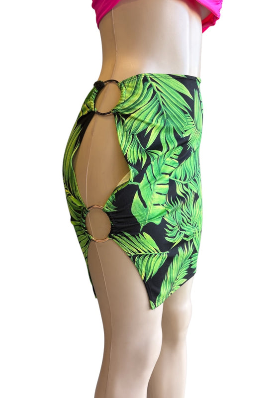 A mannequin torso wearing a green tropical leaf print mini skirt with side cutouts and gold-tone ring hardware, shown against a plain white background.