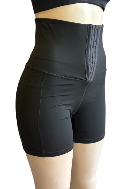 Black high-waisted compression shorts with a structured waistband and front hook-and-eye closure, shown on a mannequin against a white background.
