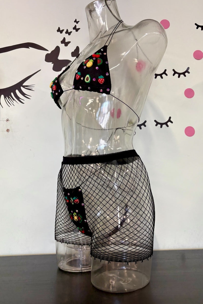 Black fishnet lingerie set with a small multicolor charm print on the bra and panty, displayed on a clear plastic mannequin torso against a white wall with decorative eyelashes and pink dots.