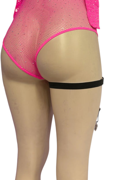 A black thigh-high leg garter with a silver bell dangle, shown on a beige mannequin leg wearing a pink mesh bodysuit.