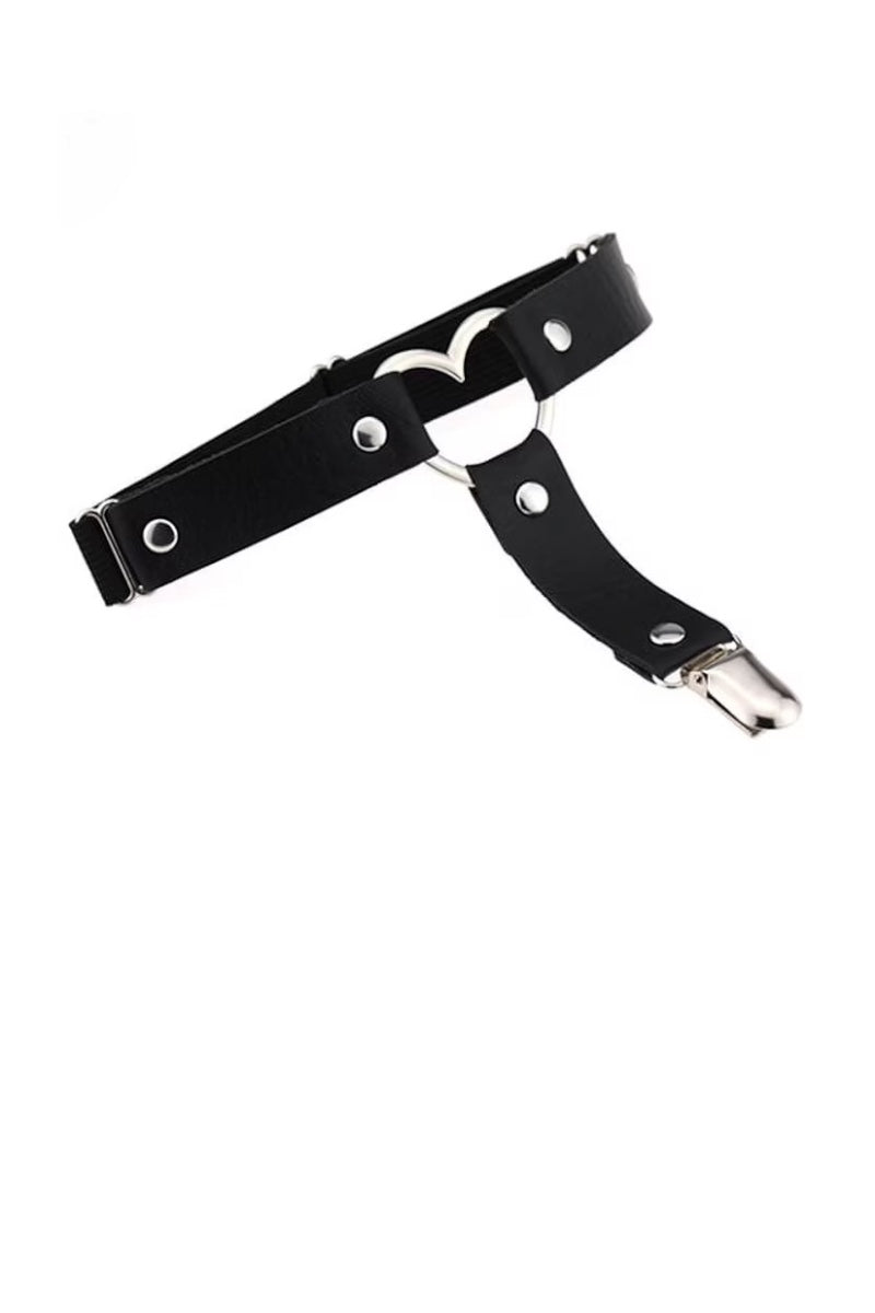 A black faux-leather harness-style belt with silver-tone metal hardware, including rivets, a heart-shaped ring, and a snap hook clasp, shown on a plain white background.