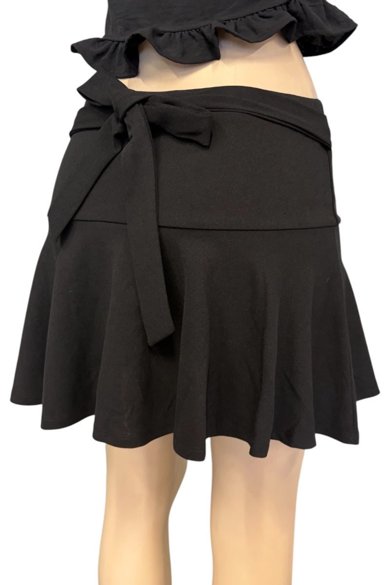 Black wrap-style mini skirt with a ruffled hem and side tie, shown on a mannequin against a white background.