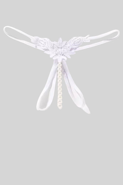 A white thong with a central floral applique, a dangling pearl bead strand, and thin elastic leg straps, shown against a solid gray background.