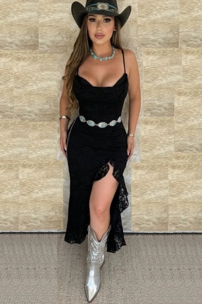 Woman in a black dress with silver cowboy boots and hat against a beige wall.