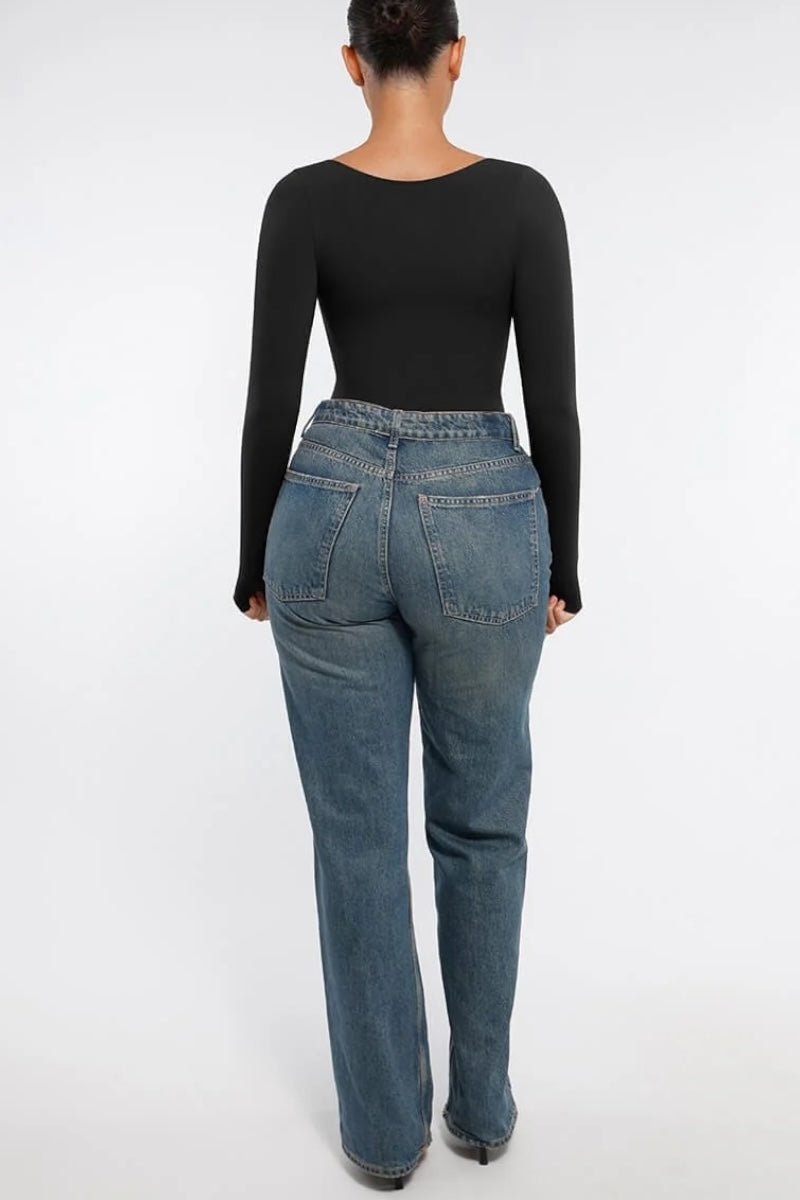 Person wearing blue jeans and a black long-sleeve top on a white background