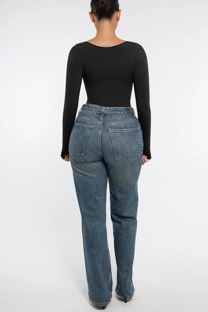 Person wearing blue jeans and a black long-sleeve top on a white background