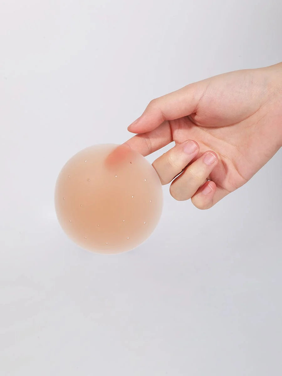 Hand holding a silicone nipple cover pad against a plain background
