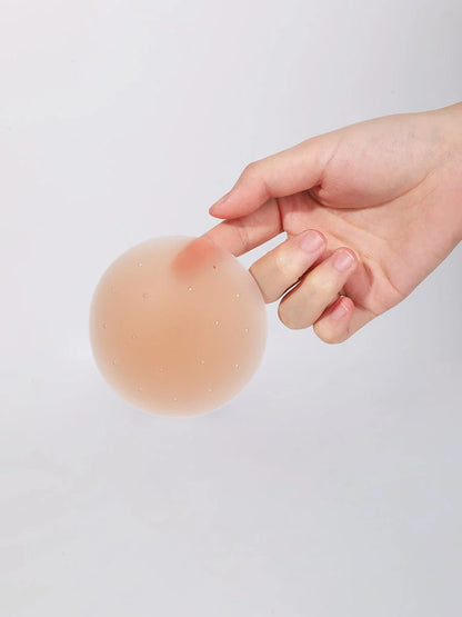Hand holding a silicone nipple cover pad against a plain background