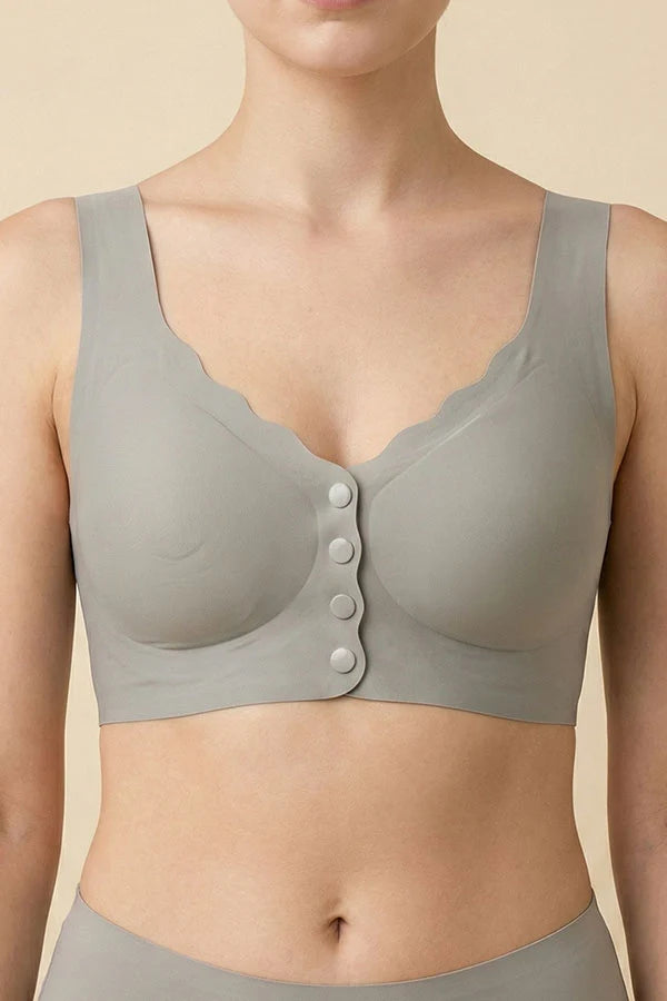 A close-up of a model wearing a light gray wireless bralette with scalloped edges and a front button closure, set against a solid beige background.