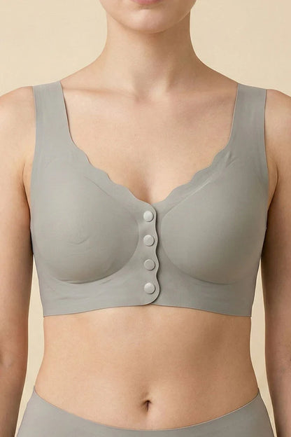 A close-up of a model wearing a light gray wireless bralette with scalloped edges and a front button closure, set against a solid beige background.
