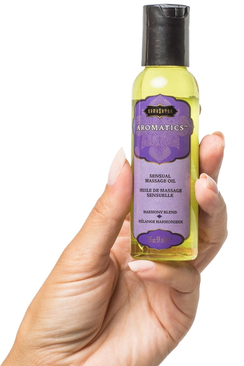 Hand holding a bottle of Kama Sutra Aromatics Sensual Massage Oil with a white background